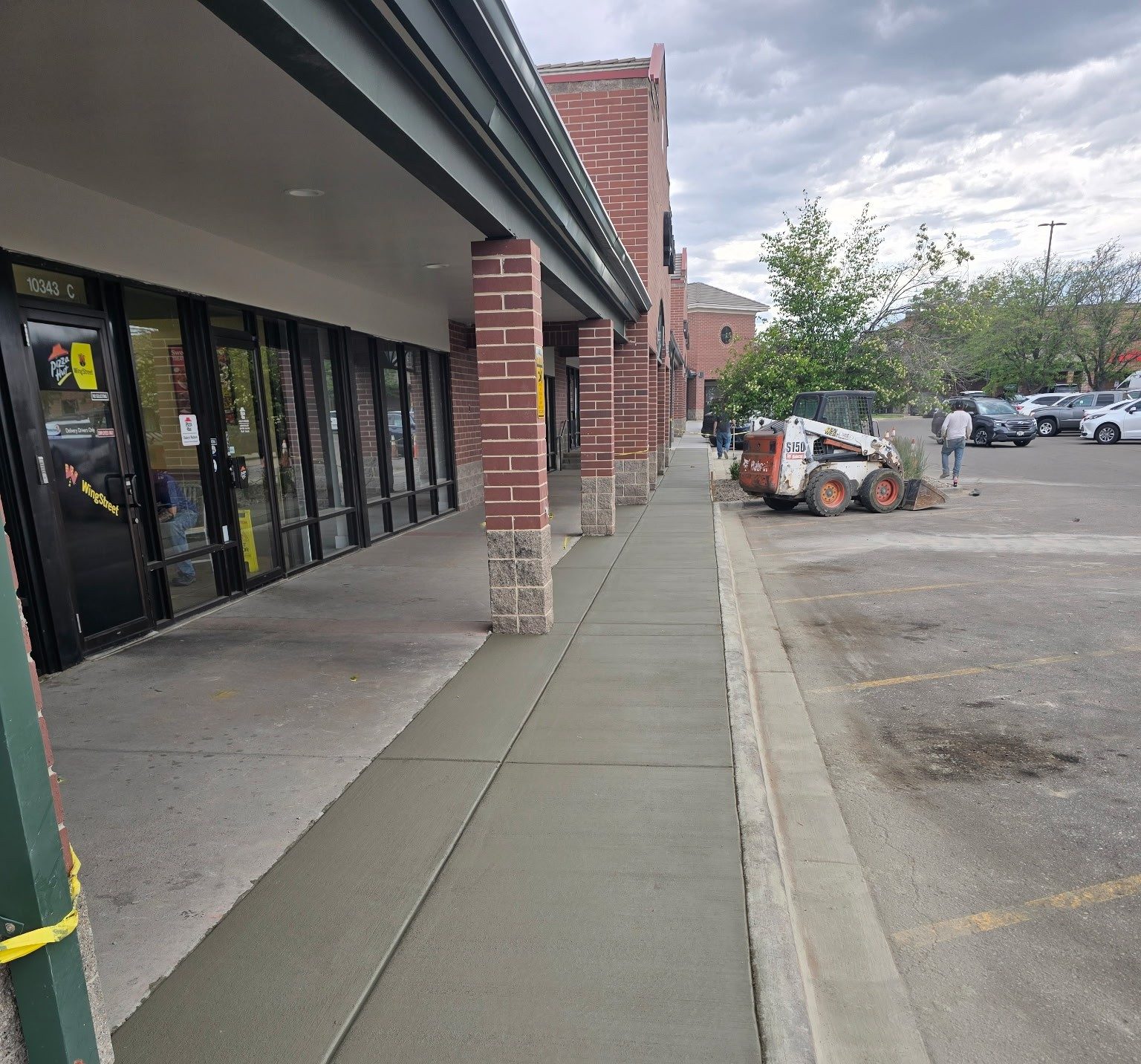 Freshly poured concrete sidewalk at a commercial property with Gen West skid steer on site